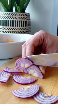 Close-up of a hand finely dicing purple red onion on a round wooden cutting board
