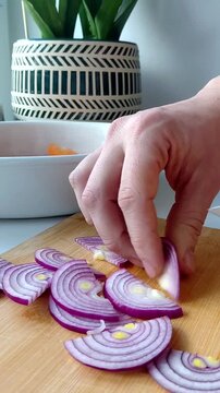Close-up of a hand finely dicing purple red onion on a round wooden cutting board