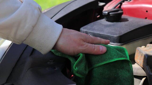 Man hand cleaning car engine bay with microfiber cloth, wiping dust under hood outdoors, car maintenance and care, checking and refilling windshield washer fluid, auto service concept, vehicle