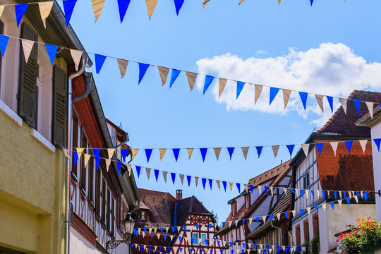 Decorative flags hang between buildings in a small street during a sunny day