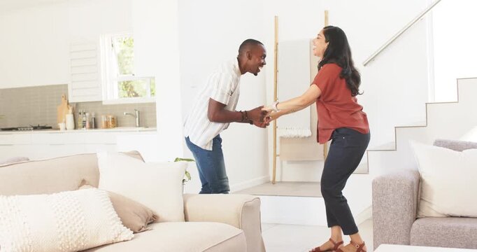Diverse couple grasping hands, stepping and dipping on step near couch, sharing affection