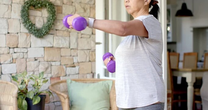 Senior Asian woman starting raising arms on patio with purple dumbbells for mobility, copy space