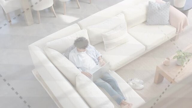 Man sitting on L-sofa working remotely typing on laptop while dashed overlays crossing laptop