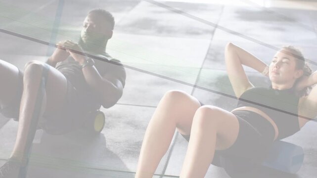 Woman initiating crunches from foam roller while man holding balance, both training core in gym