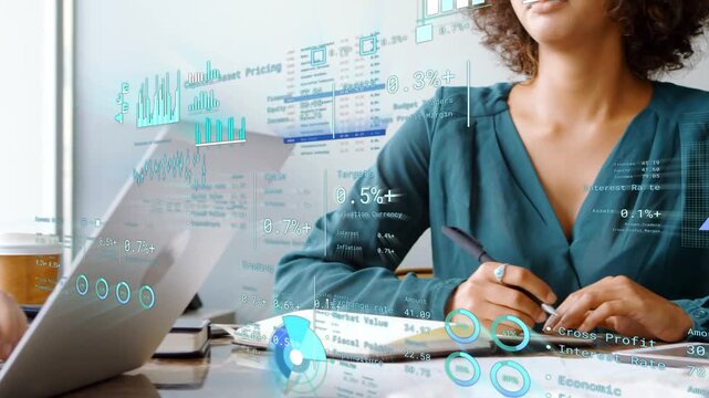 Woman writing in pad starting finance charts overlaying table while peer typing for reviewing data