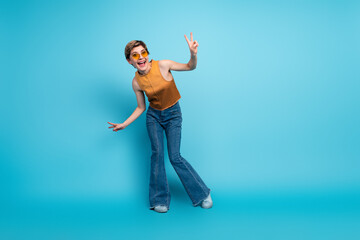 Obraz premium Young stylish woman in orange top and jeans posing with peace sign against blue background