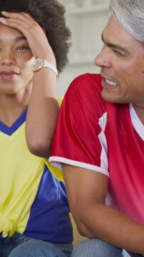 Vertical video: Reacting to offscreen cue, pair in yellow-red jerseys talking at home green bottle