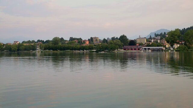 Sunrise over Lake Varese with calm water and canoe in distance, scenic b-roll footage of Gavirate lakeshore in Lombardy, Italy, peaceful early morning landscape