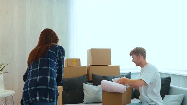 Caucasian joyful man and woman just moved in a new apartment packing their stuff and clothes. Cardboard boxes. Excited homeowners. Moving day. Happy wife and husband settled down together. Real time