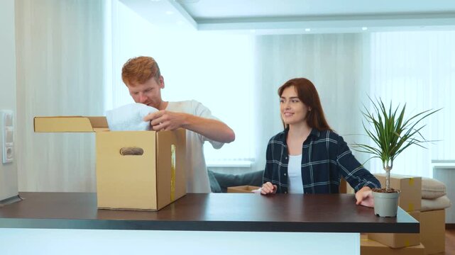 Portrait of young couple living together in new home. Couple unpacking stuff from cardboard box after moving in a new apartment. Happy spouses purchased flat. Moving day. Family concept. Real time