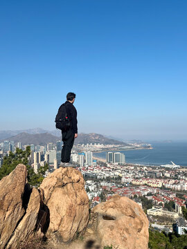 Man standing back on Fushan mountain overlooking Qingdao city and coast, China