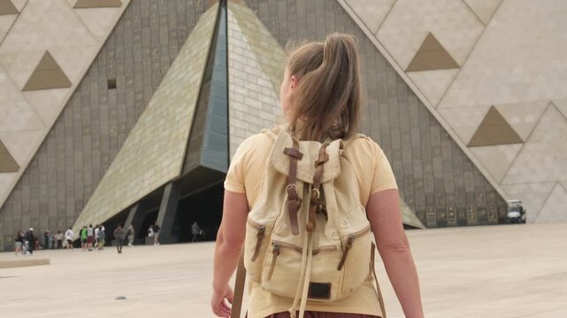 Caucasian woman tourist walking towards entrance of Grand Egyptian Museum in Giza. 
