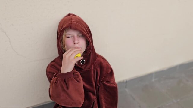 A child leaning against a wall, holding a vape. A dangerous addiction. Teen vaping its dangers and prevention
