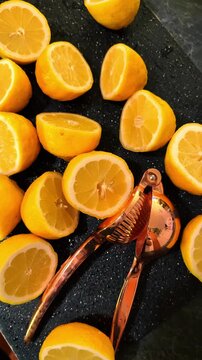 Cut lemons and citrus squeezer on dark kitchen surface. Sliced yellow lemons with copper metal manual juicer on textured black background with copy space.