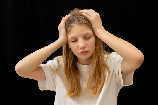 Upset Young Girl Holding Her Head. Studio portrait of a worried young girl holding her head with eyes closed against a black background.