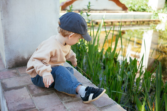 Toddler boy exploring pond plants while sitting by water in sunny park