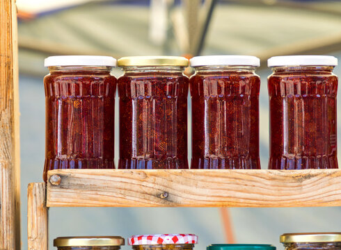Organic homemade strawberry jam in glass jars on wooden shelf sold outside on local market stall