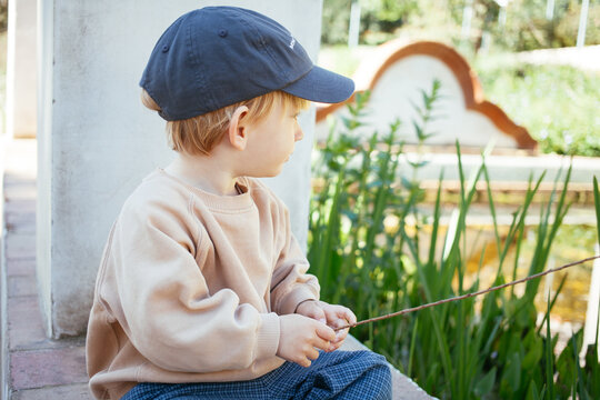 Close up of Toddler boy exploring pond plants while sitting by water in sunny park watching dugs