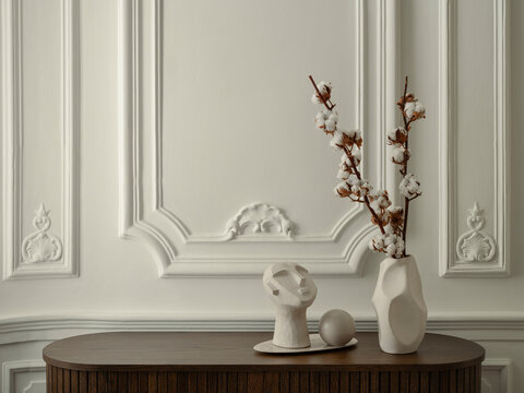 Elegant interior decor with cotton branches in a geometric vase and sculptural elements on a dark wood console table, classic wall panel details
