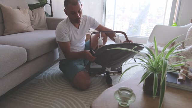 Man preparing for fatherhood by assembling a newborn baby bouncer in his modern living room