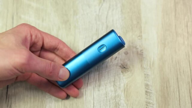 Man connecting electronic tobacco heating device to a charger, with the indicator light turning on to signal the charging process.