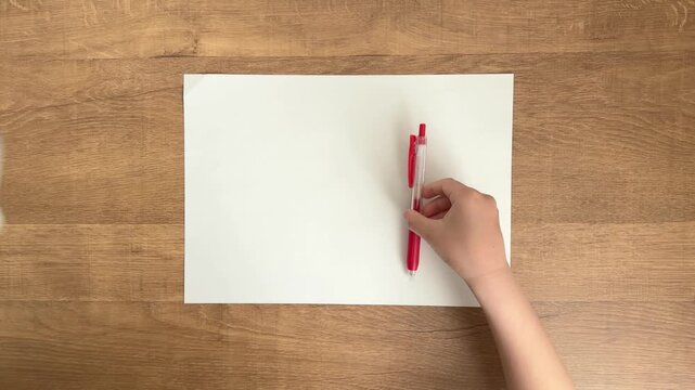 child hands placing red ballpoint pen on white paper on wooden table slow motion 4K