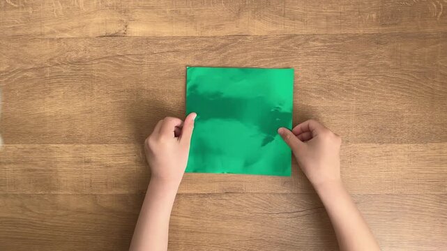 child hands placing green origami paper on wooden table slow motion 4K