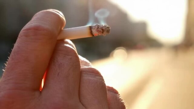 A Close-up of a Hand Holding a Cigarette with Smoke Wisps Against a Sunlit Background, Capturing the Essence of Urban Life and Quiet Moments