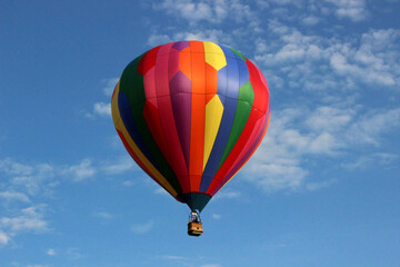 Obraz premium Multicolored striped hot air balloon with geometric panels in blue sky