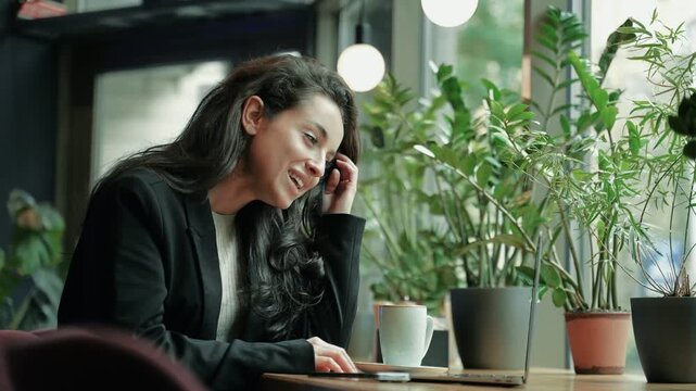 Happy beautiful woman sitting in cosy cafe while looking at laptop screen on video call and waving. Smiling lady using laptop for making video call. Technology concept. Real time