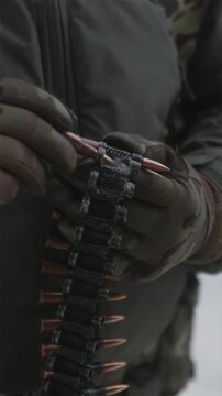 Detailed close up of soldiers hands preparing machine gun ammunition belt outdoors in snow