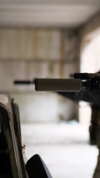 Soldier aiming and firing rifle with suppressor in abandoned building