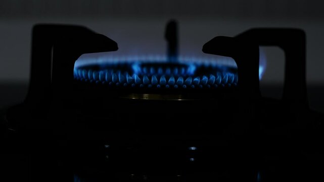 Close up lit gas stove burner with vibrant blue flame on dark background, kitchen cooking heat and fire detail, energy concept for culinary, home cooking and appliance video backdrop