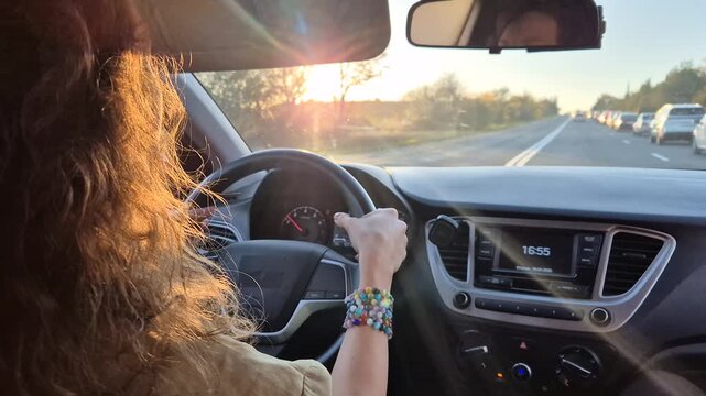 Driving traffic sunset: woman navigating highway during golden hour commute or road trip.