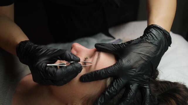 Esthetician in black gloves performing eyebrow correction procedure on a client in a beauty salon