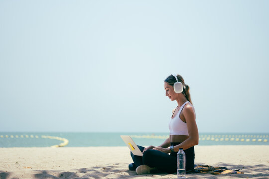 Side view of fit woman using laptop while sitting on the sand at a tropical beach