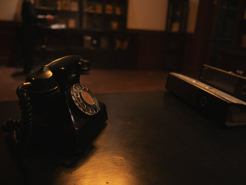 Vintage rotary telephone on wooden desk in dimly lit interior, nostalgic communication concept