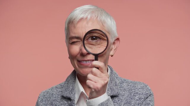 Senior Woman Looking Through Magnifying Glass on Pink