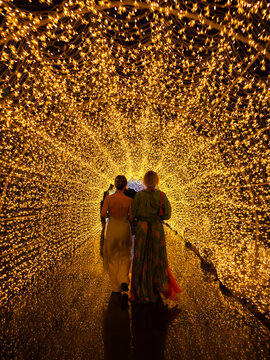 Two women walking through glowing golden light tunnel at night, immersive illuminated pathway and magical experience concept