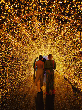Two women walking through glowing golden light tunnel at night, immersive illuminated pathway and magical experience concept