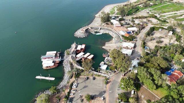 Cinematic drone tilt-down into Ein Gev harbor with traditional wooden boats at the Sea of Galilee marina, Israel