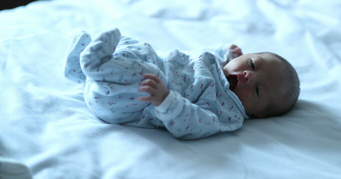 Newborn baby awake on bed spreading legs and arms, first week of life