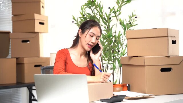 Focused Entrepreneur: An entrepreneur, immersed in the rhythm of her work, engages in a phone call while meticulously documenting details, amidst stacks of packages