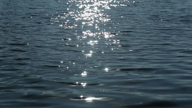 Wide horizontal shot of open sea with bright sunlight forming long glittering trail across rippling water surface, sparkles shift and scatter continuously in natural daylight.