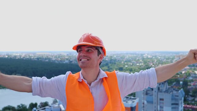 Young male builder wearing construction uniform and safety helmet celebrating crazy on the roof. Business, building, industry concept. Real time