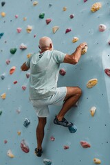 Fototapeta premium Bald man ascending indoor climbing wall during training session