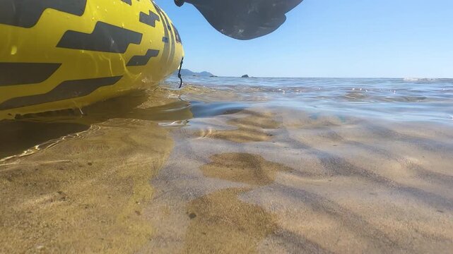 Slow motion water level view of a kayak resting on the shoreline with paddles above and gentle wave motion in clear sea under natural light