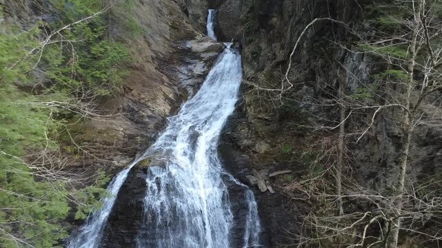 Smooth drone video of a waterfall in the forest, slowly backing away from the falls. 
