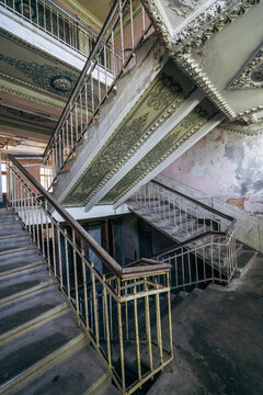 Grand ruined stairwell with metal railings, decorative ceiling, abandoned historic building, urban decay, heritage architecture, restoration concept.