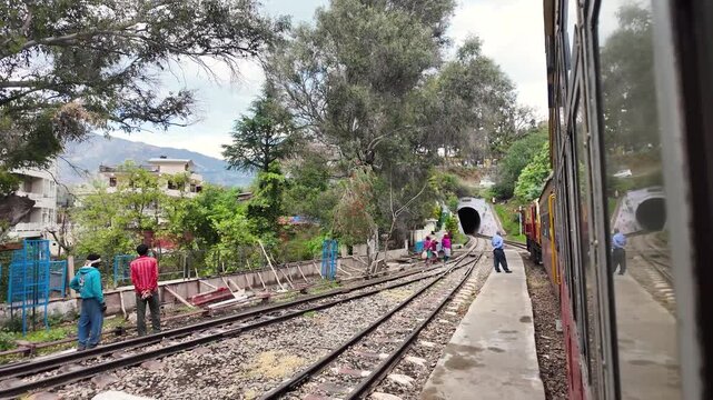 People walk cautiously across train tracks at a rural station.